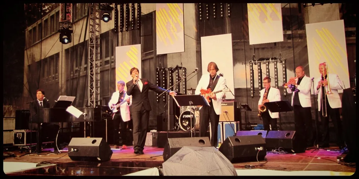 Die Band in weißen Sakkos auf einer großen Open-Air-Bühne mit Lichttraversen